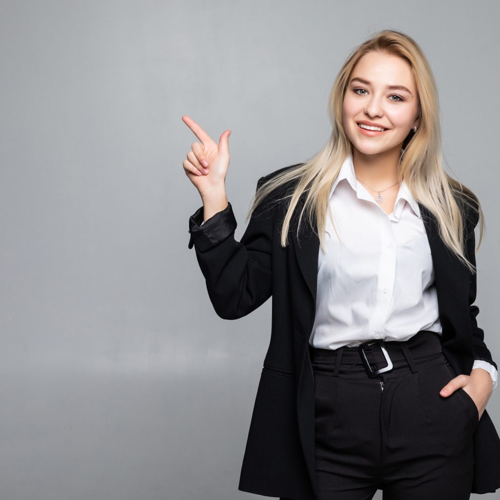 Young business woman pointing finger to the side on grey background